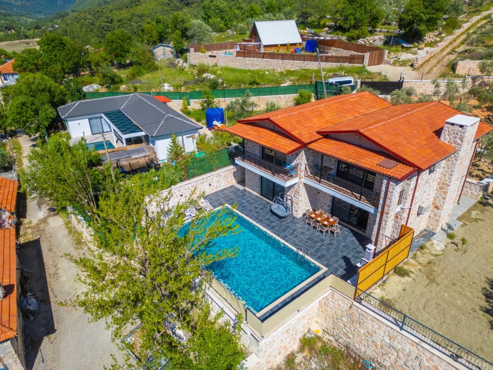 Kiremit çatılı taş villanın havuzlu bahçesi ve çevresindeki yeşil doğa.