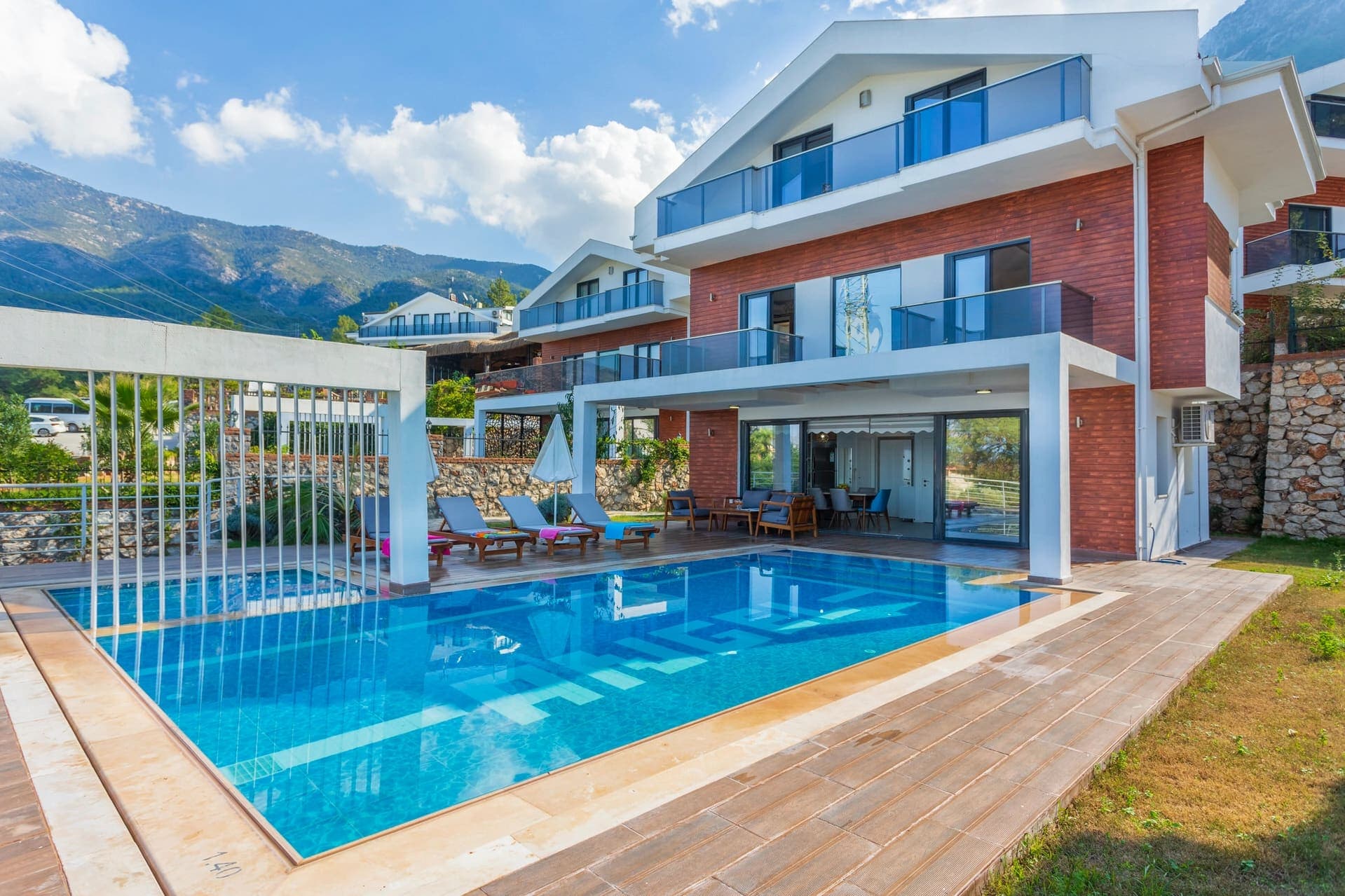 Dağ manzaralı geniş havuz ve şezlonglara sahip villanın dış cephesi.
