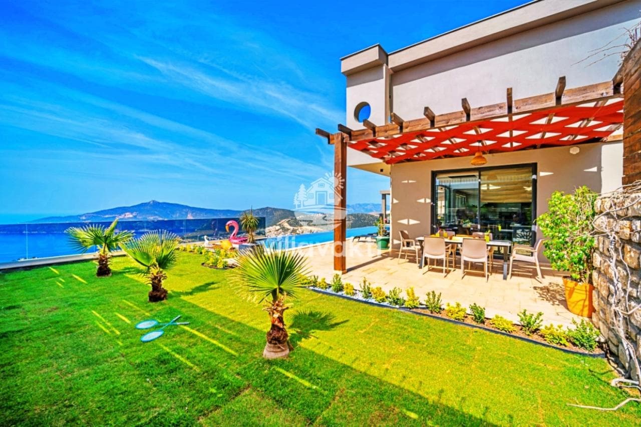 Deniz manzaralı villanın bahçesinde yeşil çim alan, palmiyeler ve gölgelikli veranda.