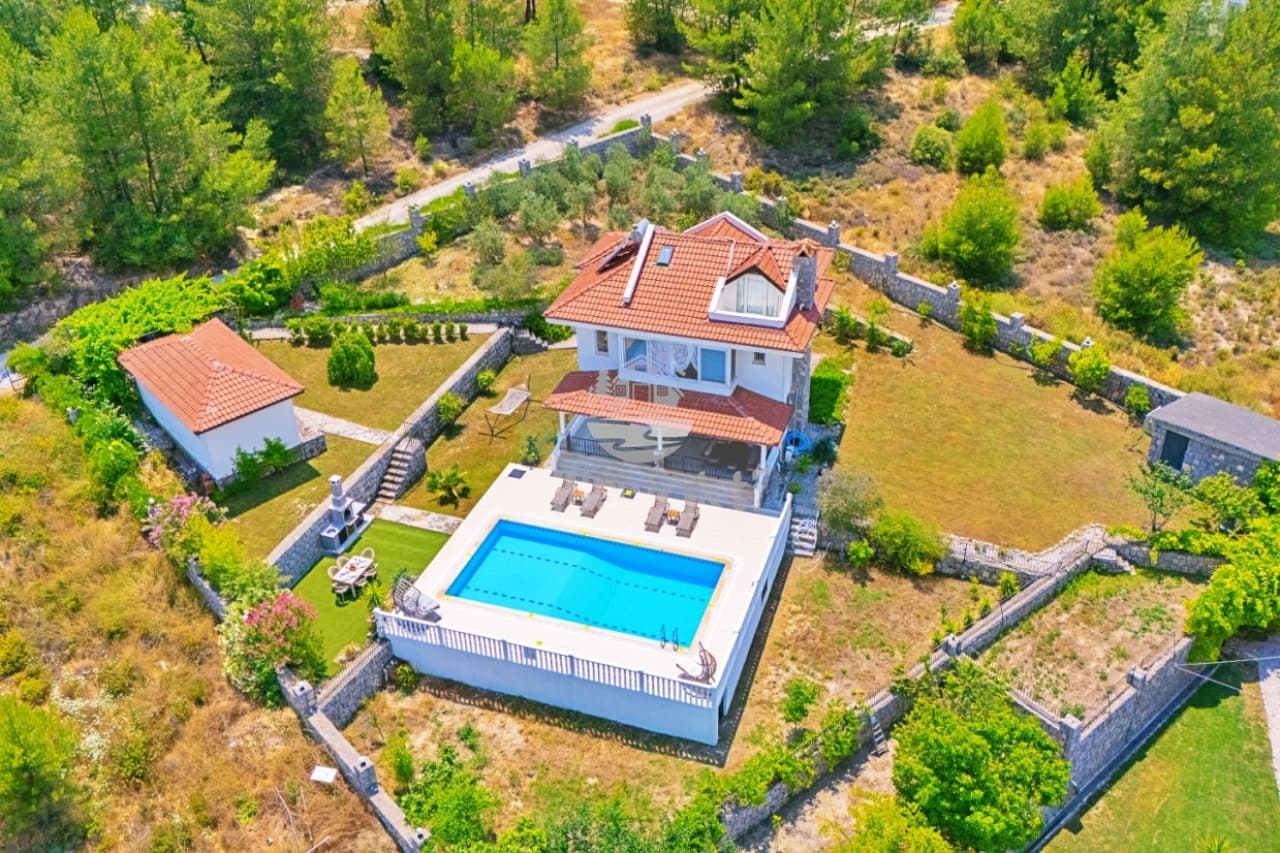 Kiremit çatılı villa, bahçesinde havuz, barbekü alanı ve çevresinde ağaçlar.