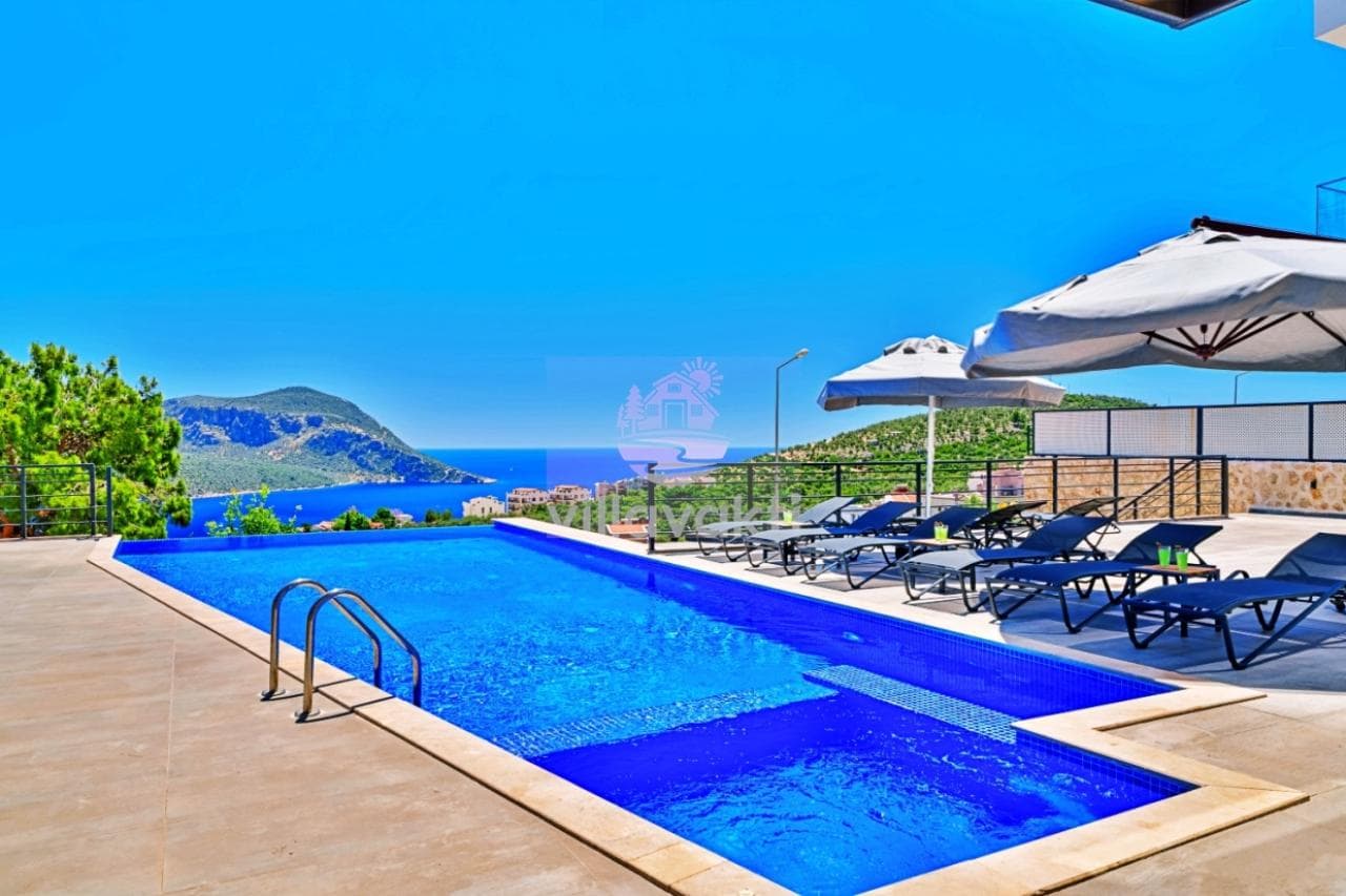 Deniz manzaralı havuz kenarında şezlonglar, güneş şemsiyeleri ve mavi bir gökyüzü.