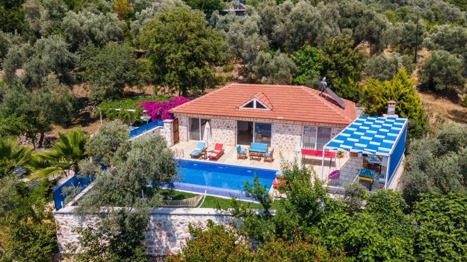 Ağaçlar arasında kalan tek katlı taş villanın havuzlu bahçesi.