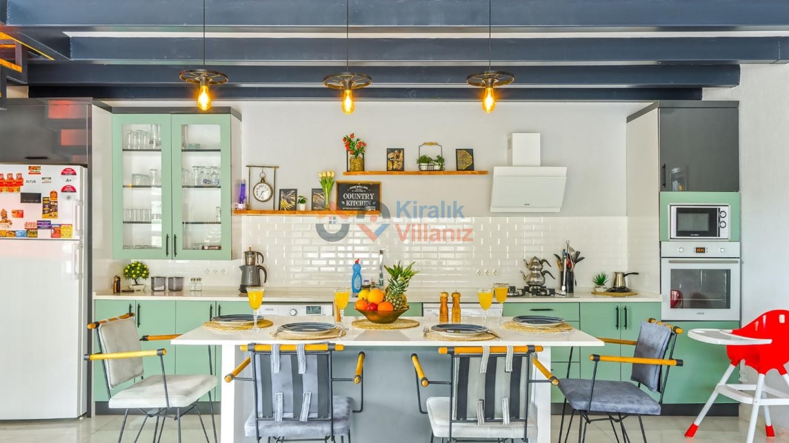 Yeşil dolaplı, beyaz tezgahlı modern mutfak ve önünde yemek masası bulunan açık planlı iç mekan.