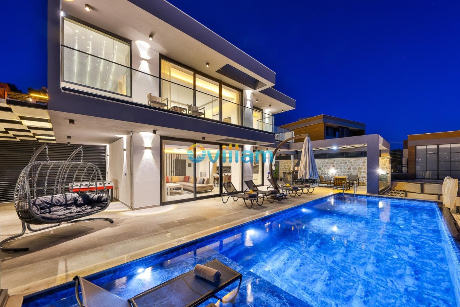 Gece aydınlatılmış modern villa, havuz başında salıncak ve oturma alanı bulunuyor.