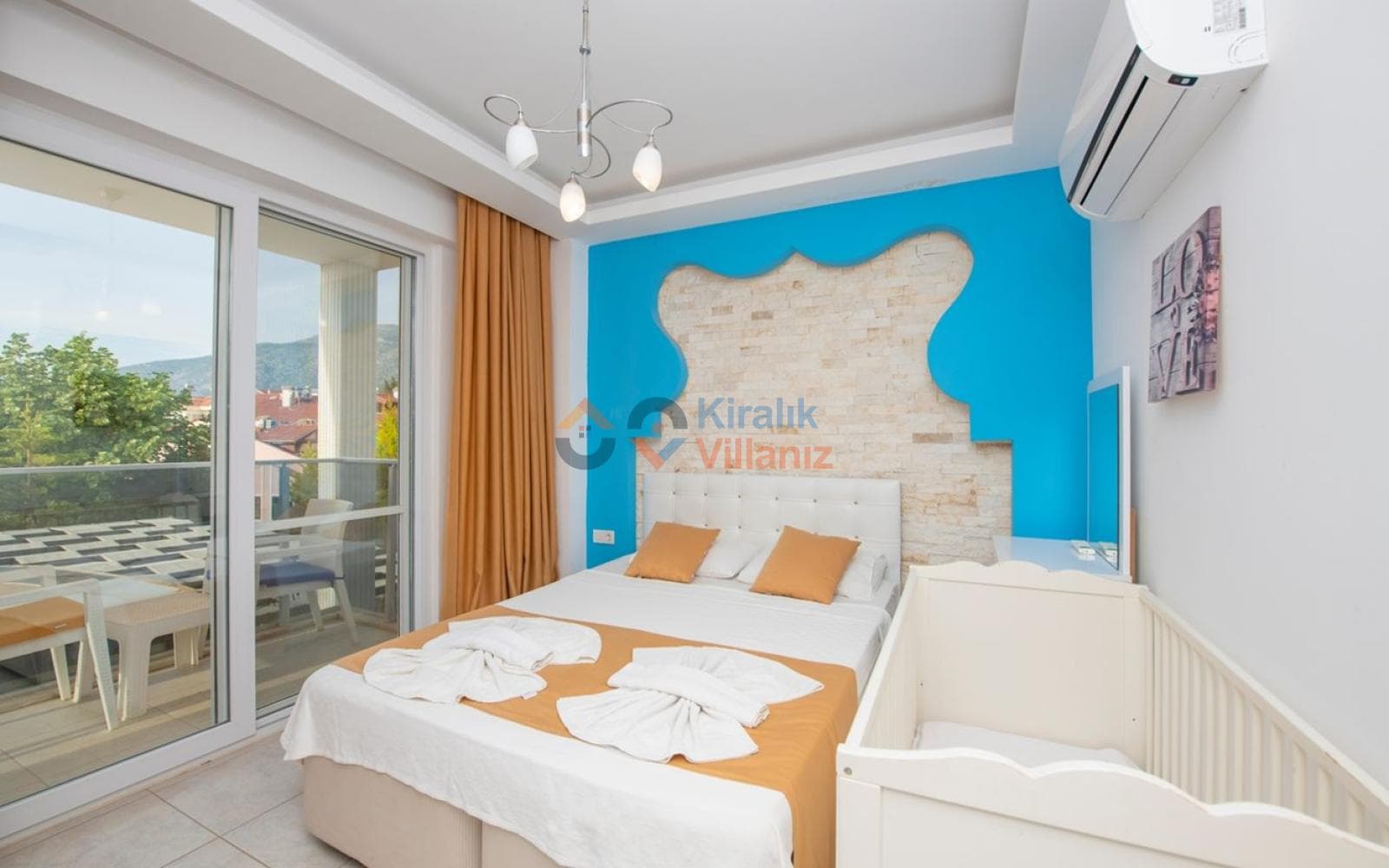 Mavi duvar detaylı, çift kişilik yatak ve yanında beyaz bebek karyolası bulunan yatak odası.