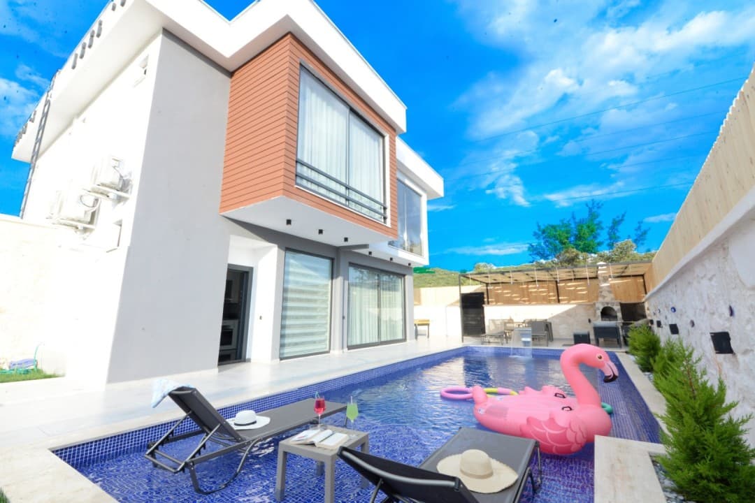Bahçesinde havuz, şezlonglar ve pembe flamingo şişme yatak bulunan modern villa.