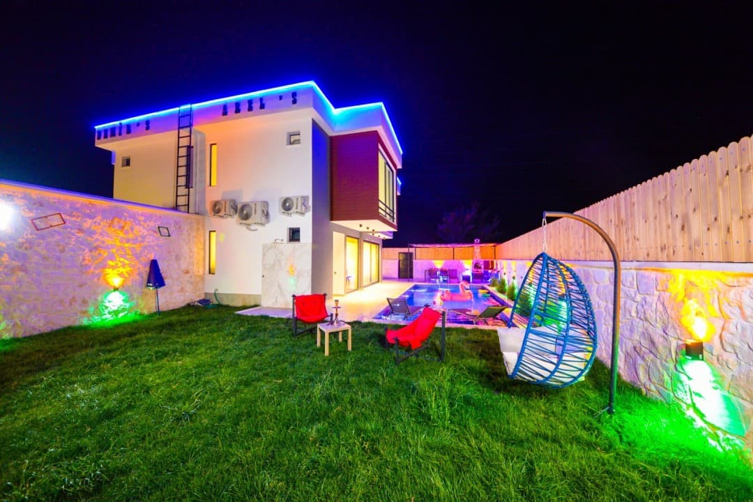 Gece aydınlatmalı, havuzlu ve bahçesinde salıncak bulunan Villa Arels'in dış görünümü.