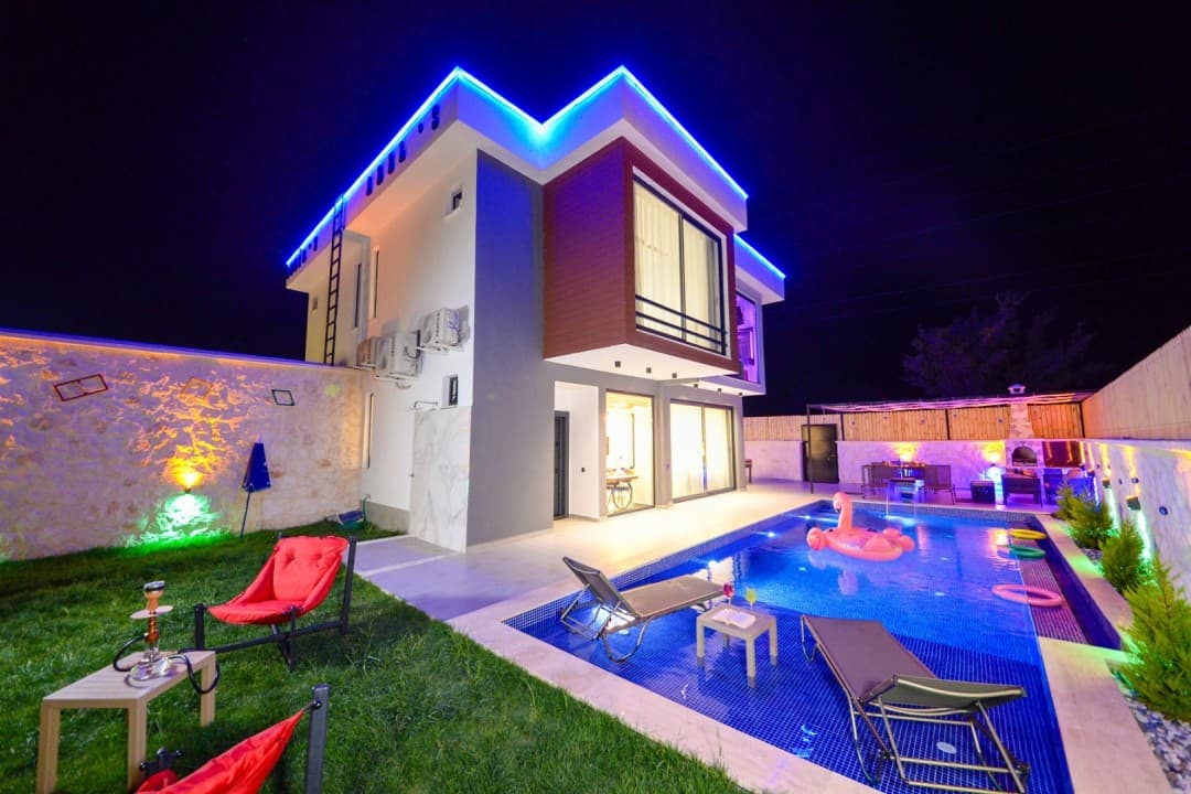 Mavi led aydınlatmalı iki katlı lüks villa, havuz ve şezlonglar.