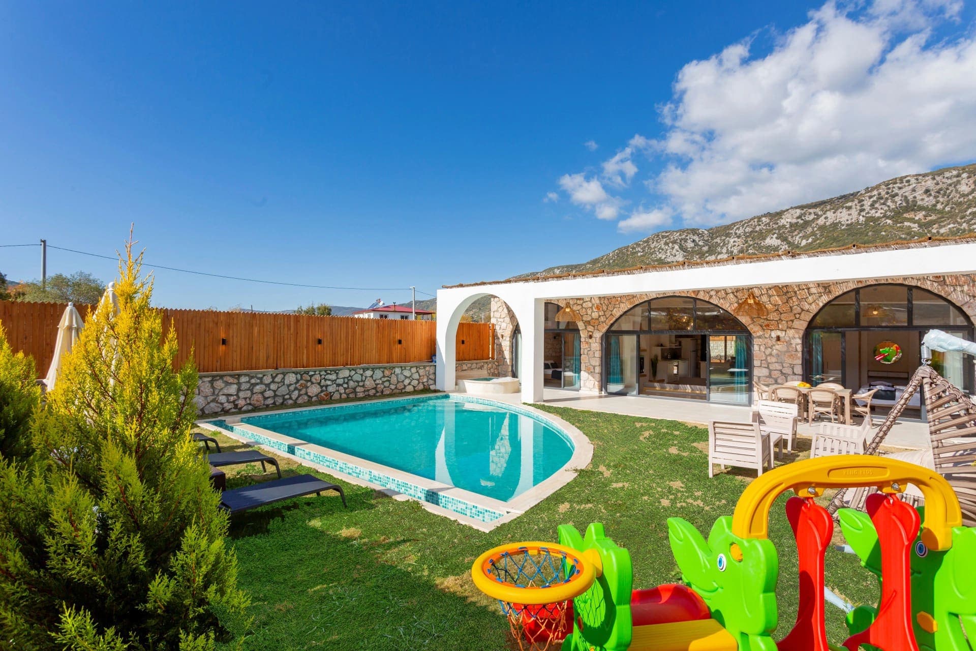 Taş kemerli pencereleri olan villa, önünde yüzme havuzu ve çocuk oyun alanı.