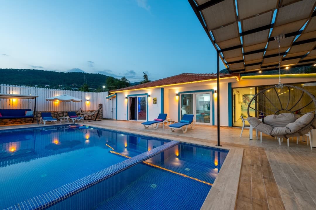 Akşam saatlerinde havuz başında şezlonglar, salıncak ve gölgelikli oturma alanı bulunan tek katlı villa.