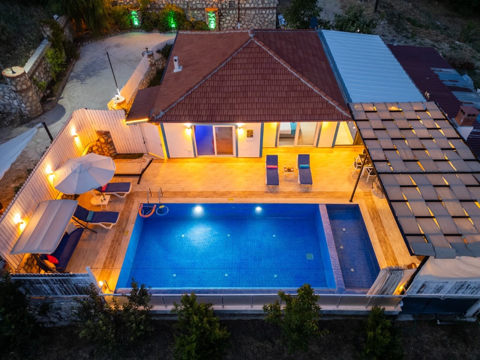 Üstten çekimde aydınlatmalı havuz, şezlonglar ve kiremit çatılı tek katlı villa