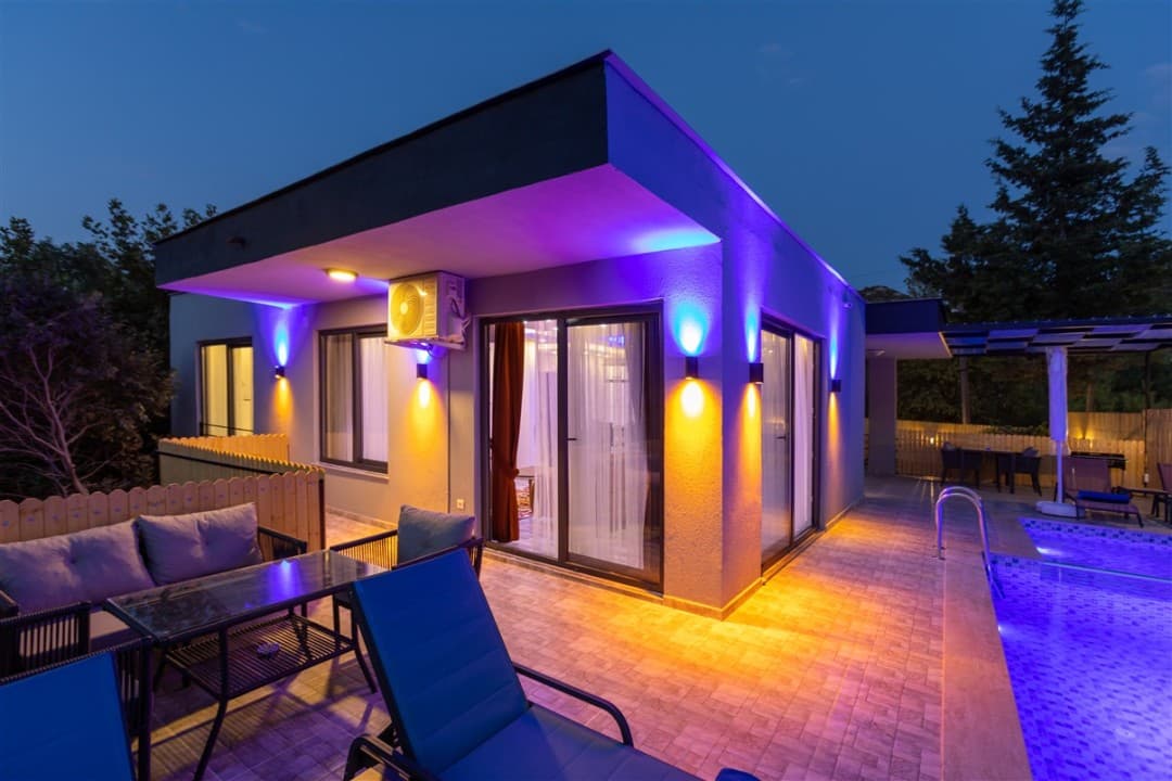 Akşam vakti aydınlatılmış, önünde havuz ve şezlonglar bulunan modern tek katlı villa.