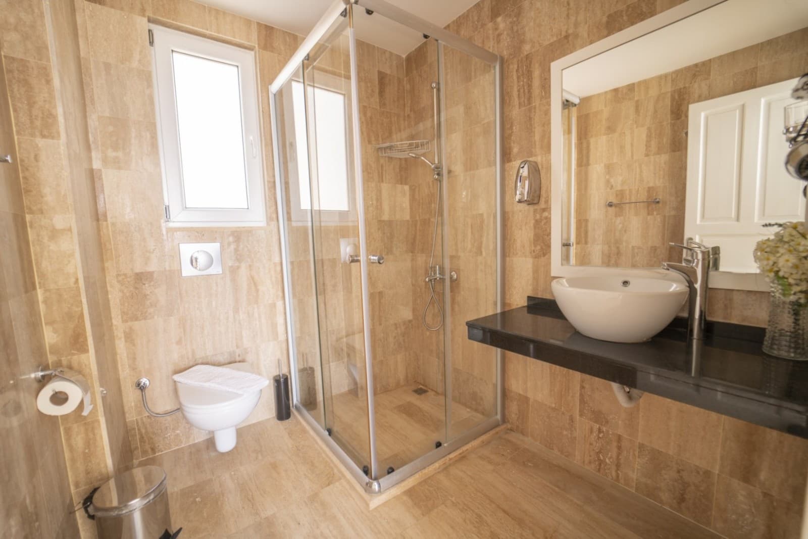 Bej seramik kaplı banyoda cam duş kabini ve aynalı lavabo.
