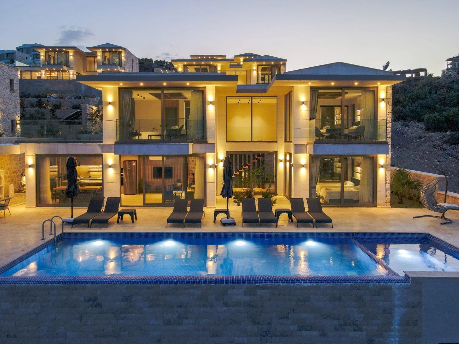 Akşam ışıklandırmasıyla aydınlanan, iki katlı modern villa ve önünde ışıklandırılmış havuz.