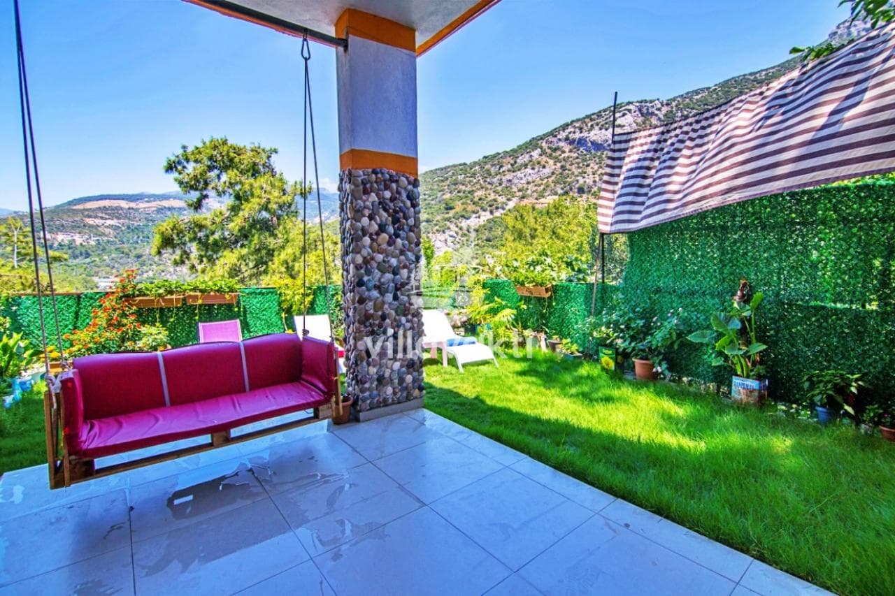 Verandada kırmızı bir salıncak, çim alan ve arka planda ağaçlıklı dağ manzarası.