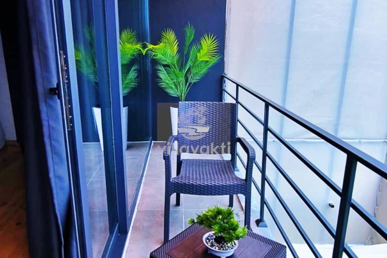 Siyah sandalyeli ve yapay bitkili, metal korkuluklu modern balkon köşesi.