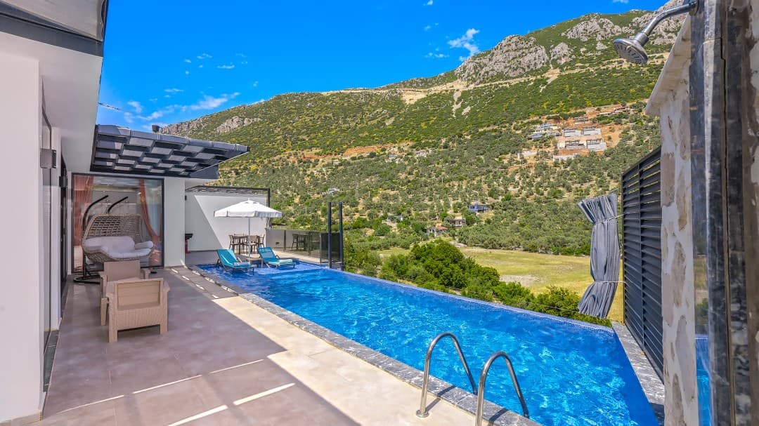 Dağ manzaralı havuz kenarında şezlonglar ve masa bulunan villa terası.