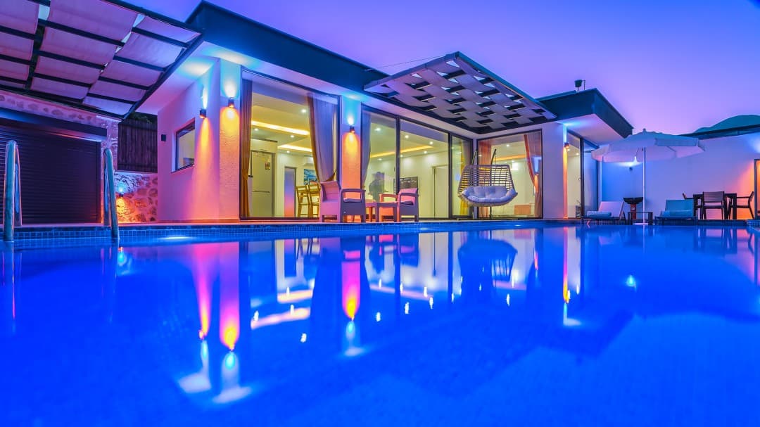 Akşam vakti mavi aydınlatmalı havuz kenarında, ışıklandırılmış modern tek katlı villa.