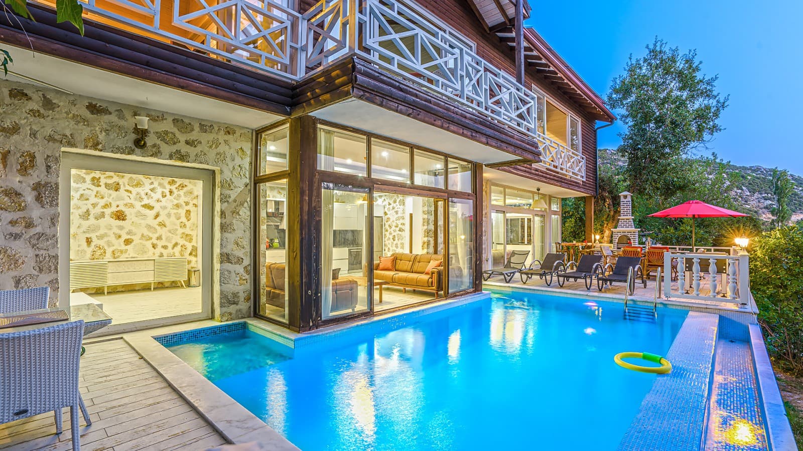 Ahşap detaylı taş villa önünde aydınlatmalı yüzme havuzu.