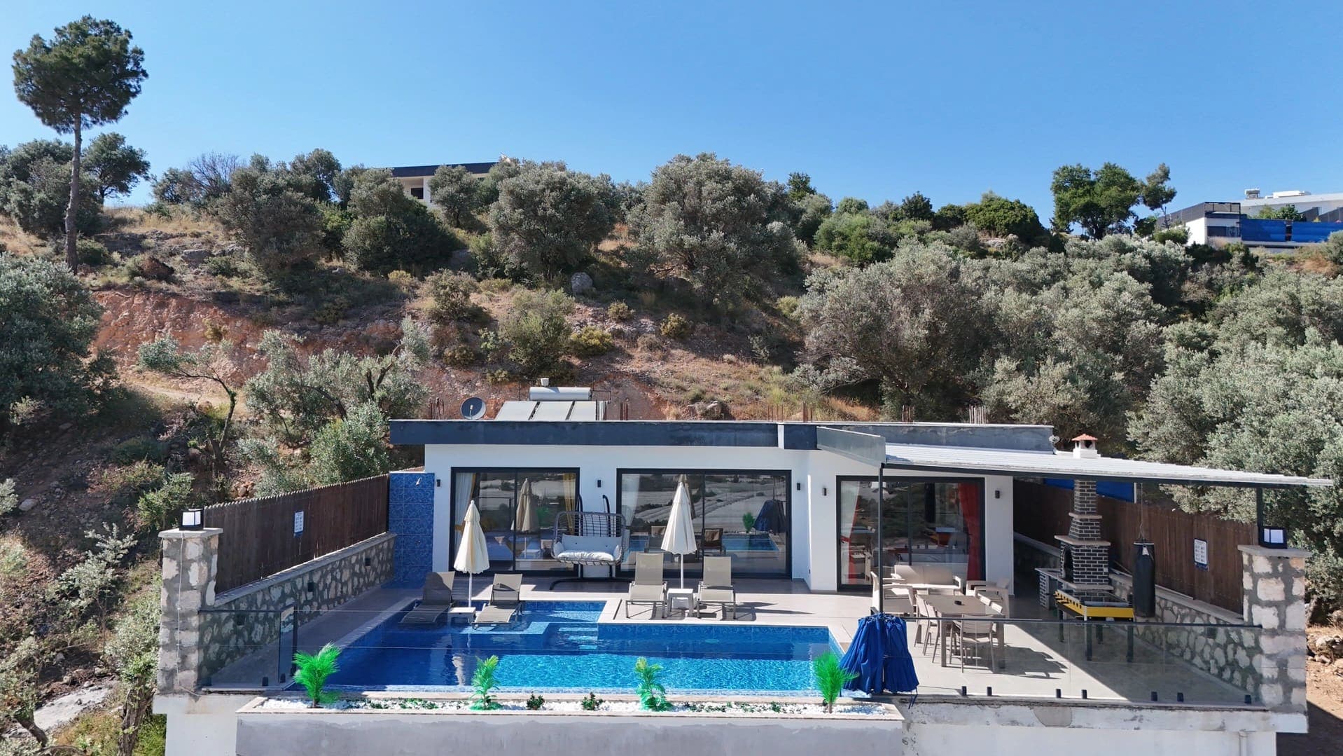Havuz terasında şezlonglar, oturma grubu ve barbekü alanı bulunan tek katlı villa.
