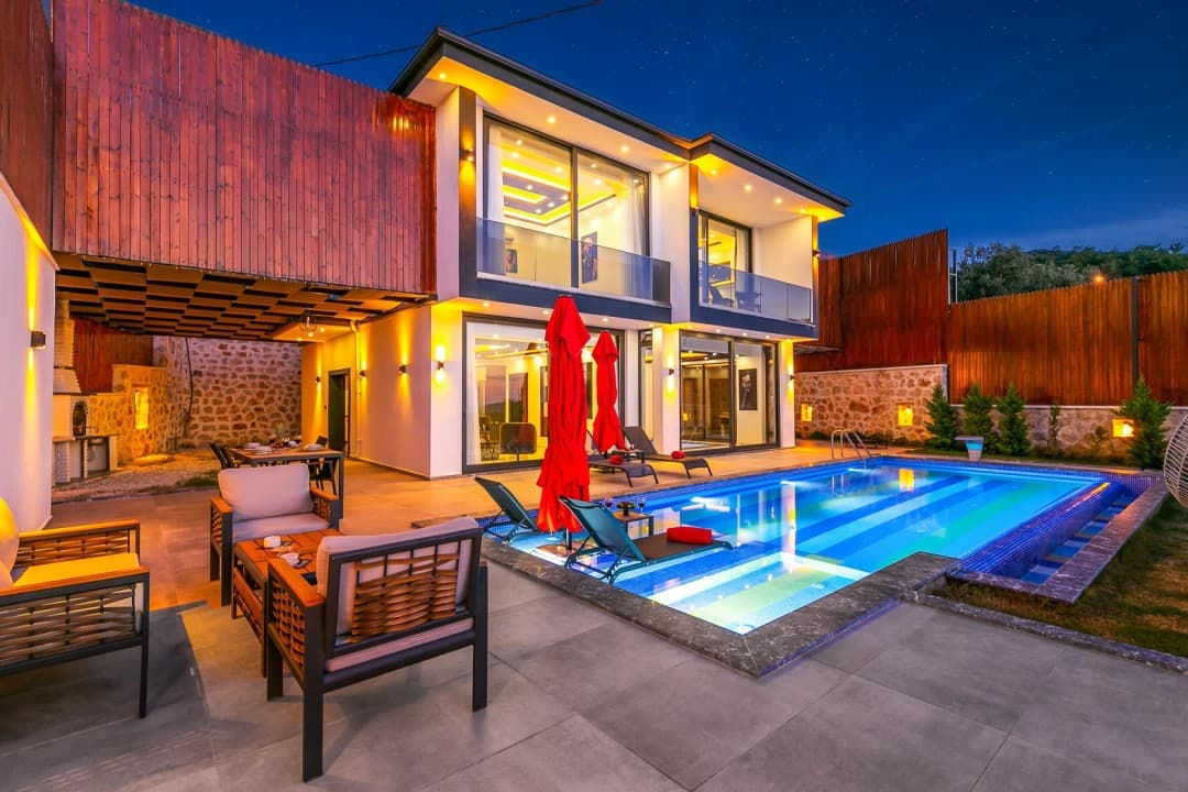 Gece aydınlatmalı, özel havuzlu, kırmızı şemsiyeli ve modern mobilyalı iki katlı müstakil villa.