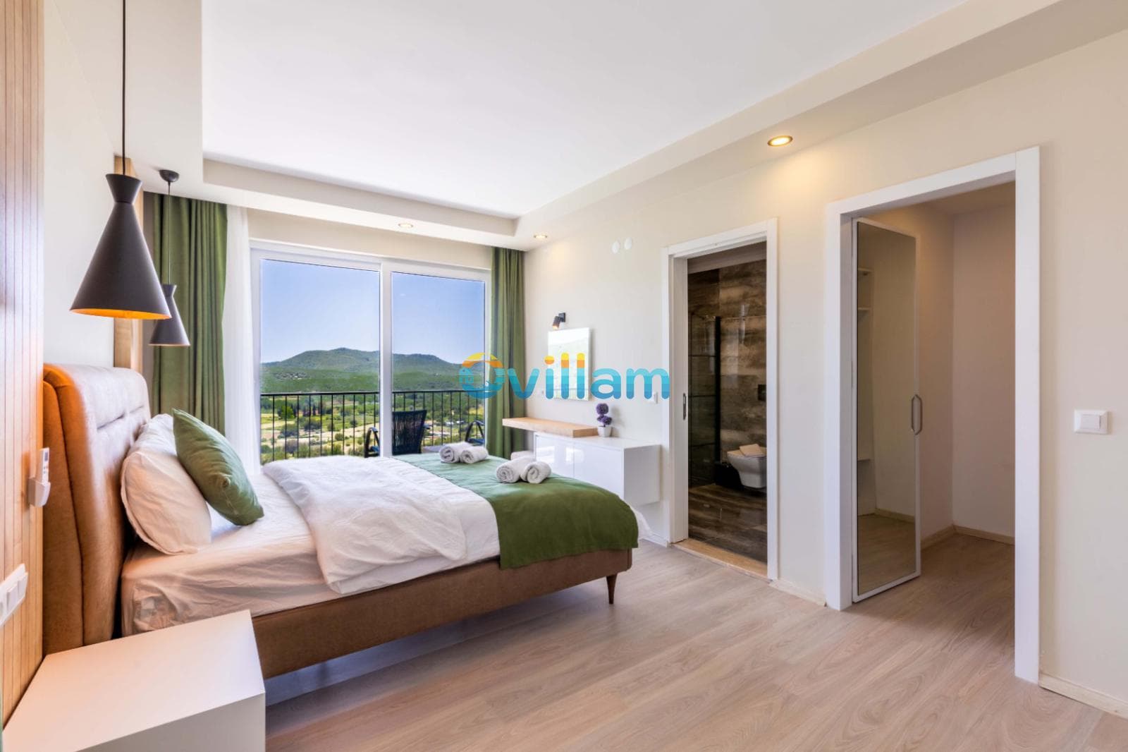 Çift kişilik yatak, yeşil örtüler, modern aydınlatma ve balkon kapısından görünen doğa manzaralı yatak odası.