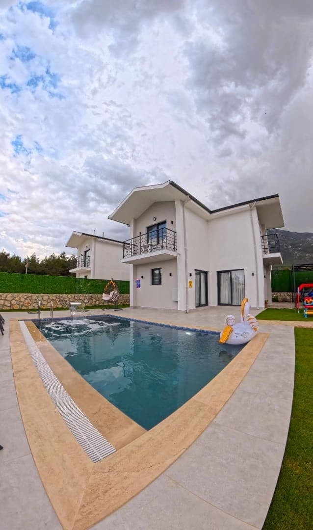 Beyaz dış cepheli iki katlı villa ve önünde içinde kuğu figürlü deniz yatağı bulunan yüzme havuzu.