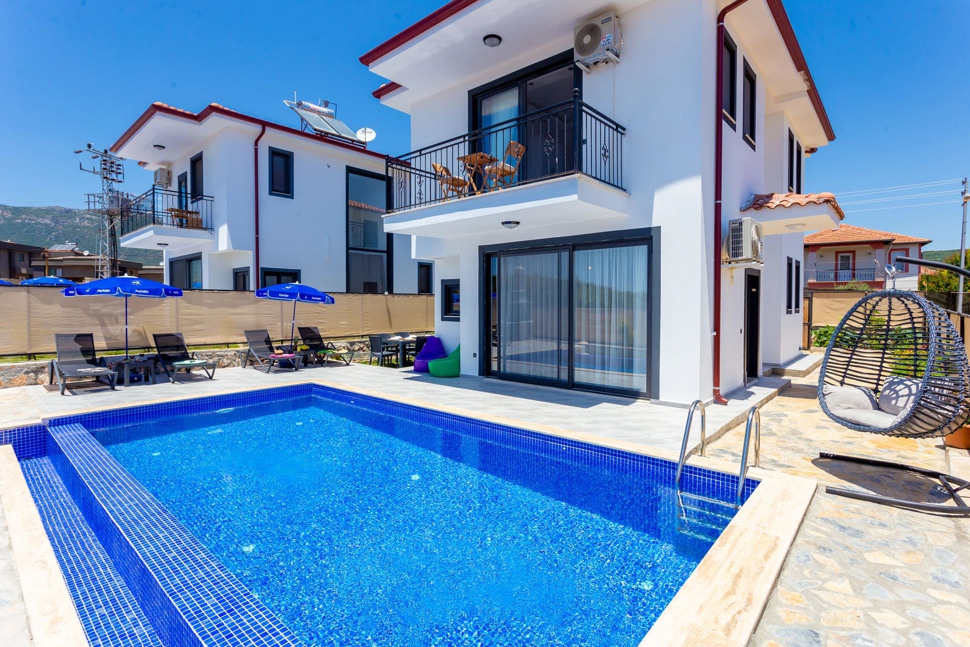 Mavi havuzlu ve şezlonglu beyaz villa dış cephesi.