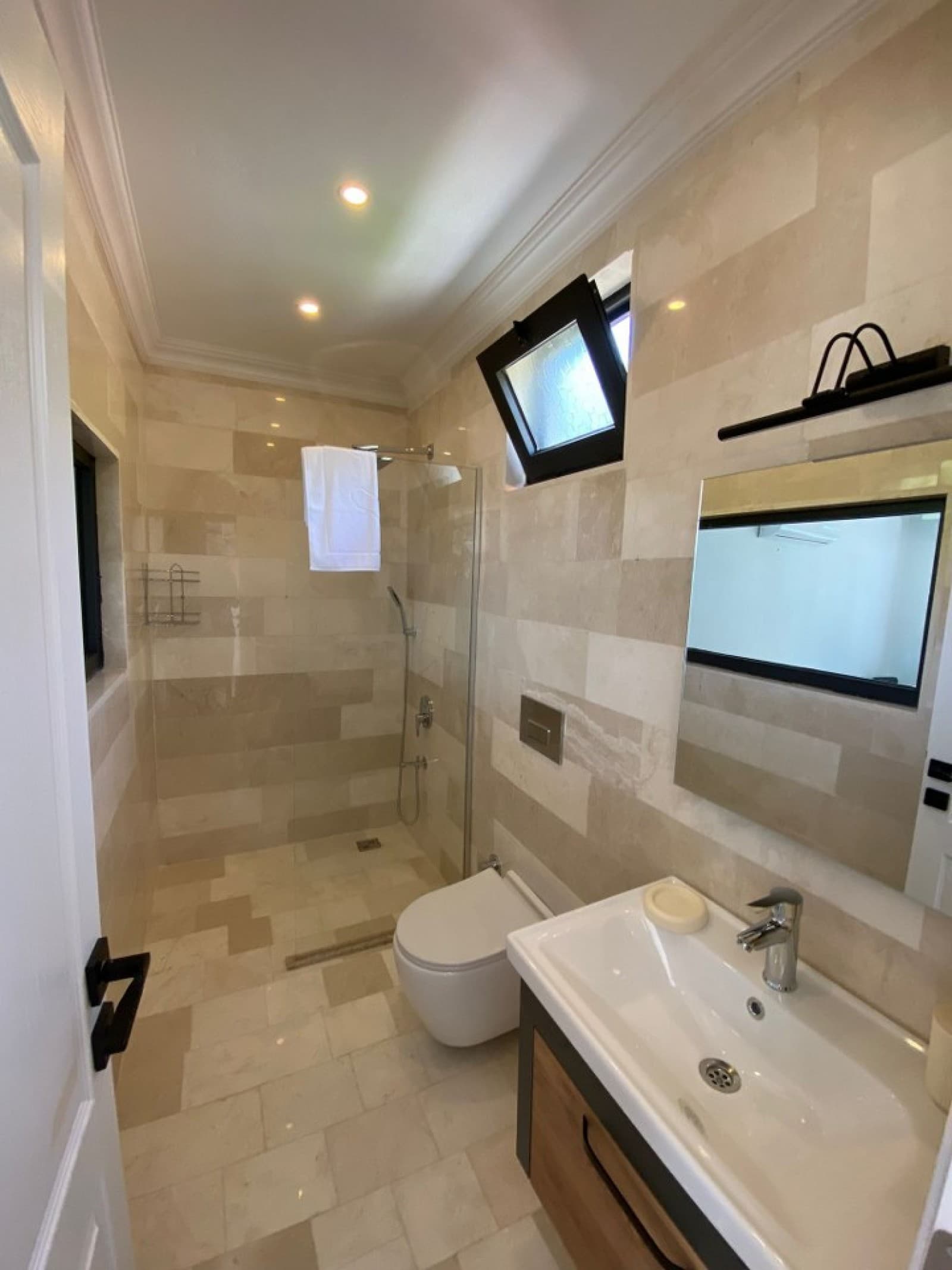 Bej tonlarında fayans kaplı banyoda duş kabini ve lavabo.