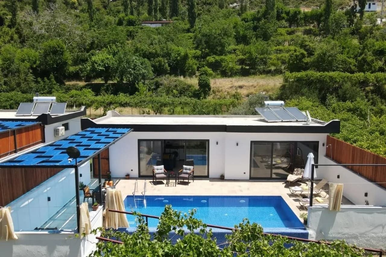 Ağaçlar arasında havuzlu ve şezlonglu bahçesi olan tek katlı beyaz villa.