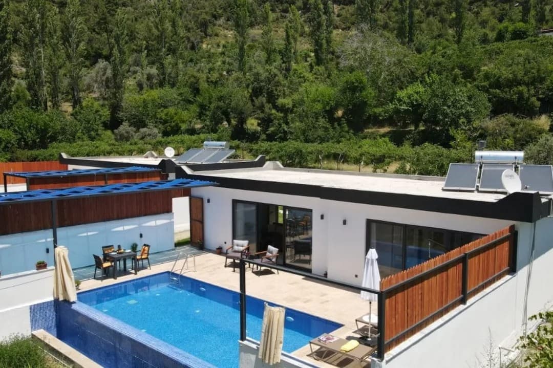 Orman manzaralı, özel havuzlu ve güneş enerjisi panellerine sahip tek katlı beyaz villa.