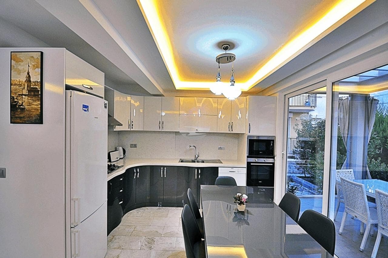 Modern mutfak ve yemek masası içeren açık plan iç mekân, tavanda gizli led aydınlatmalar mevcut.