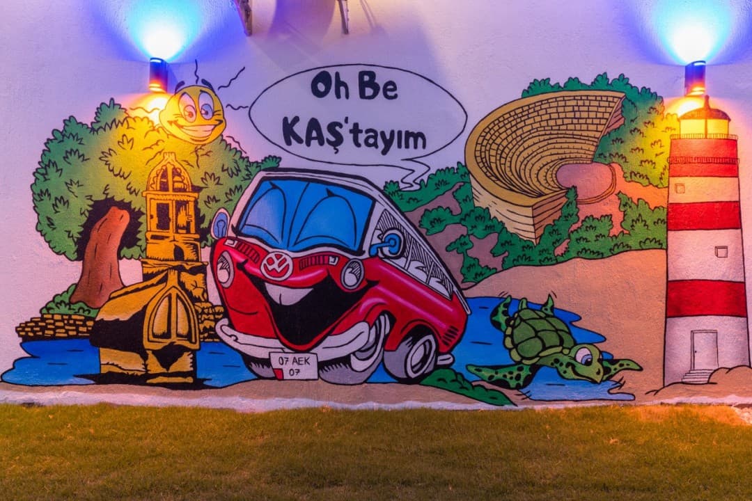 Duvara çizilmiş, üzerinde "Oh Be KAŞ'tayım" yazan kırmızı karikatür minibüs duvar resmi.
