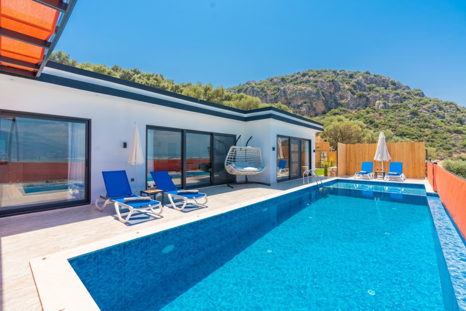 Mavi yüzme havuzu ve şezlongların yer aldığı villa terası.