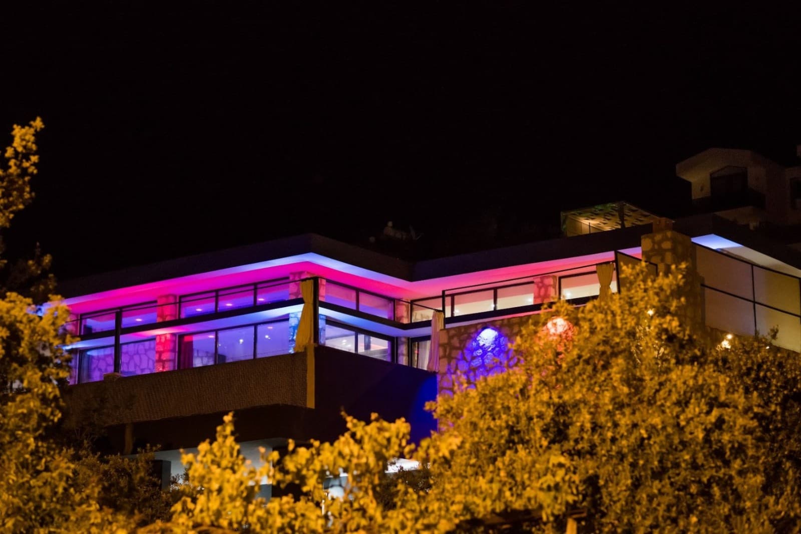 Renkli LED aydınlatmalarla ışıklandırılmış iki katlı villanın gece görünümü.