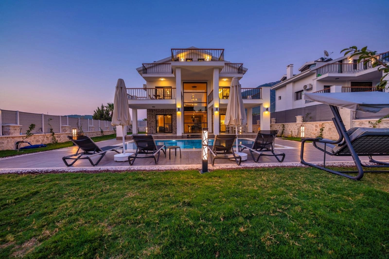 Akşam ışıklandırmalı havuzlu lüks villa dış cephesi.