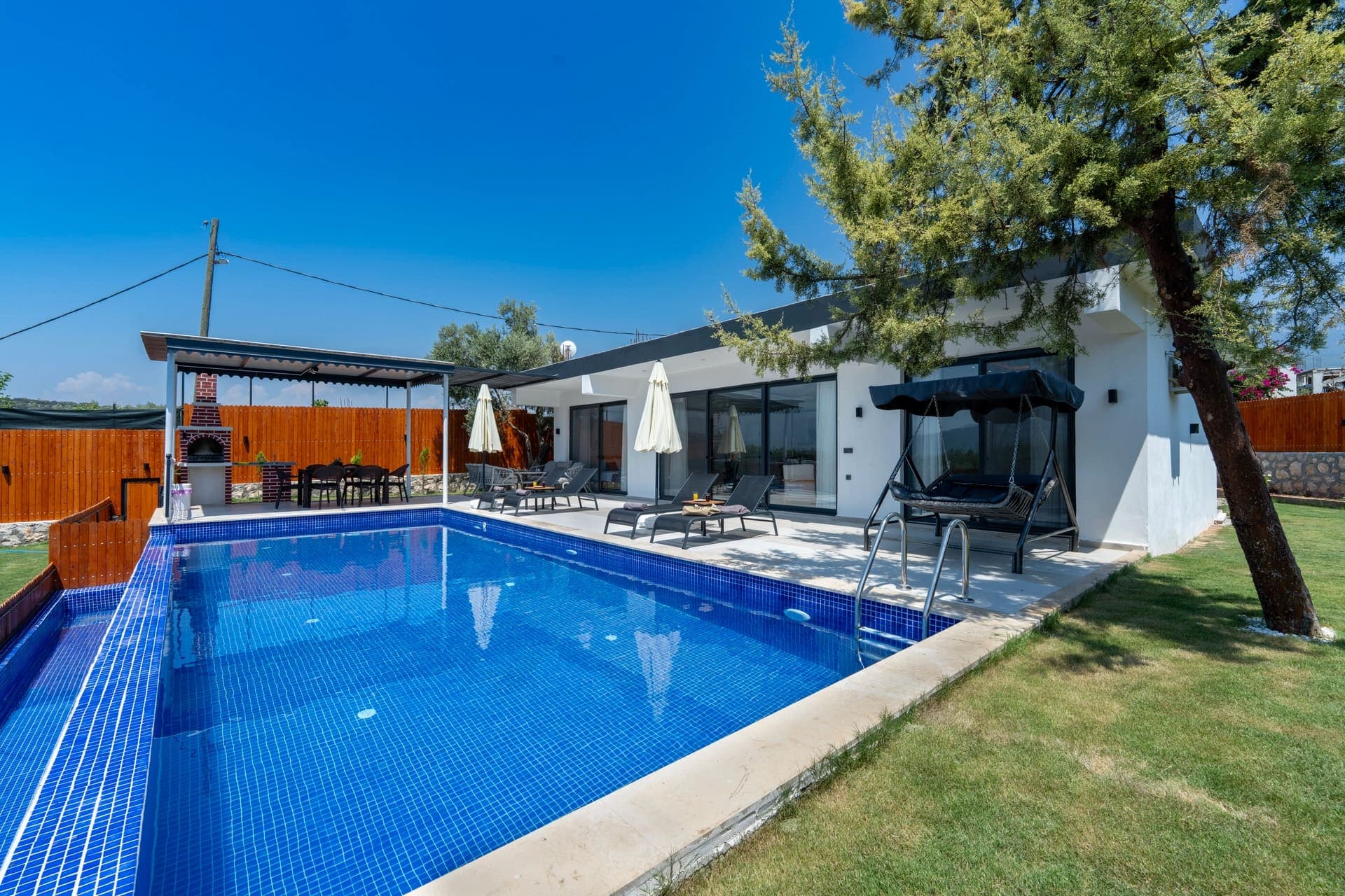 Bahçesinde havuz, salıncak ve yemek masası bulunan tek katlı villa.