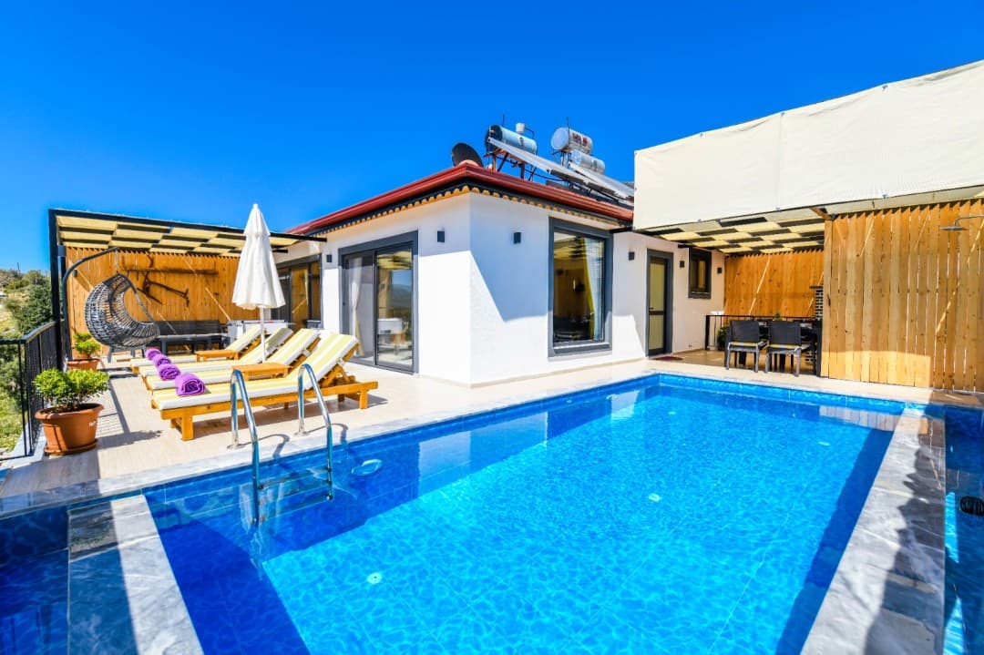 Mavi yüzme havuzu ve şezlongların bulunduğu beyaz dış cepheli villa.