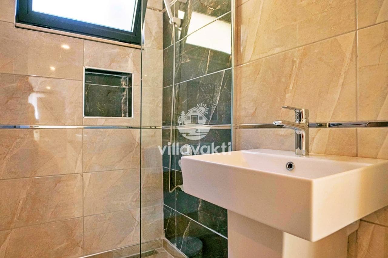 Bej mermer kaplı, cam duşakabinli ve beyaz lavabolu modern bir banyo.