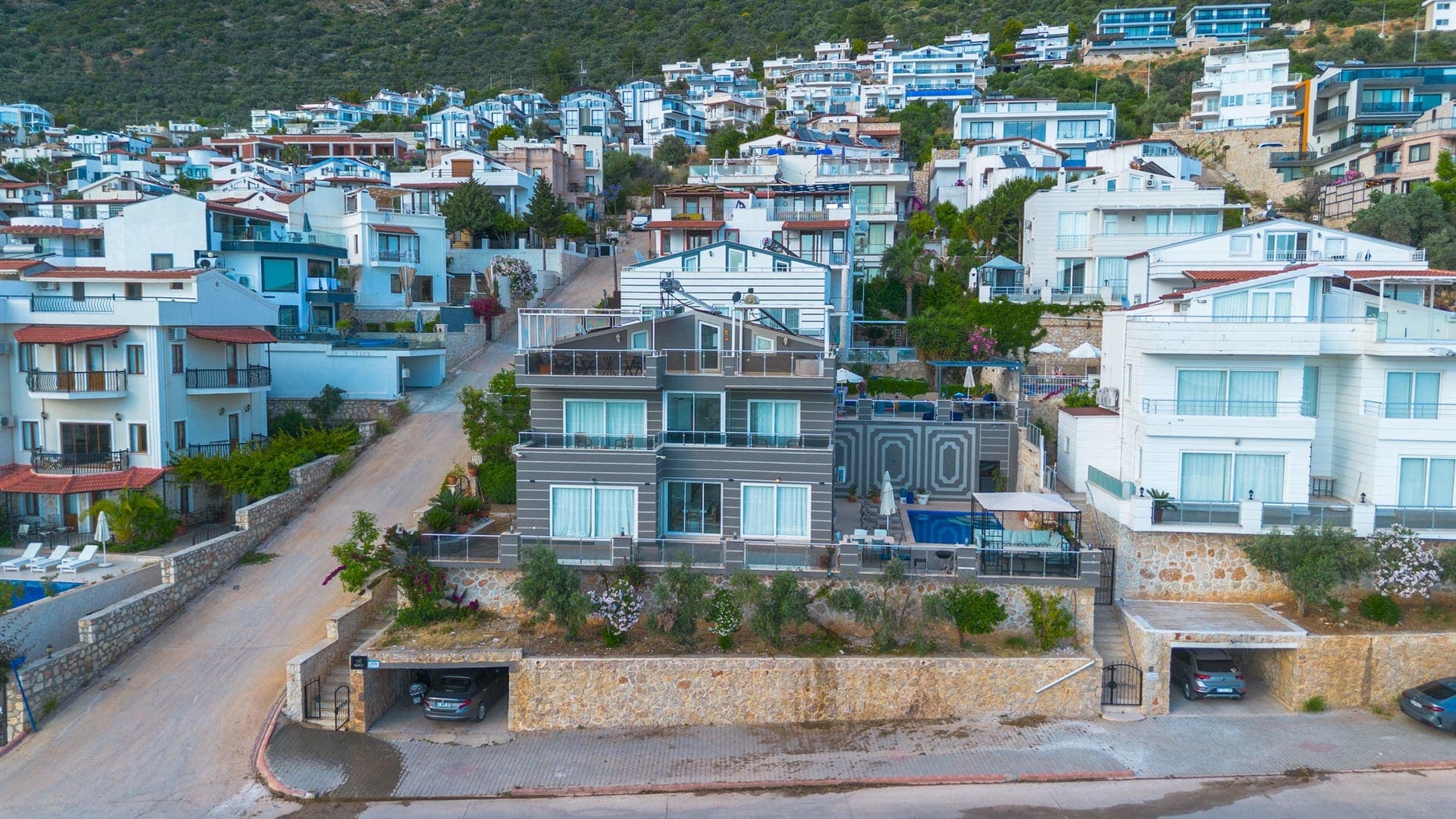Yamaçta konumlanmış, özel havuzlu ve teraslı modern villa dış cephesi ve çevresindeki yerleşim.