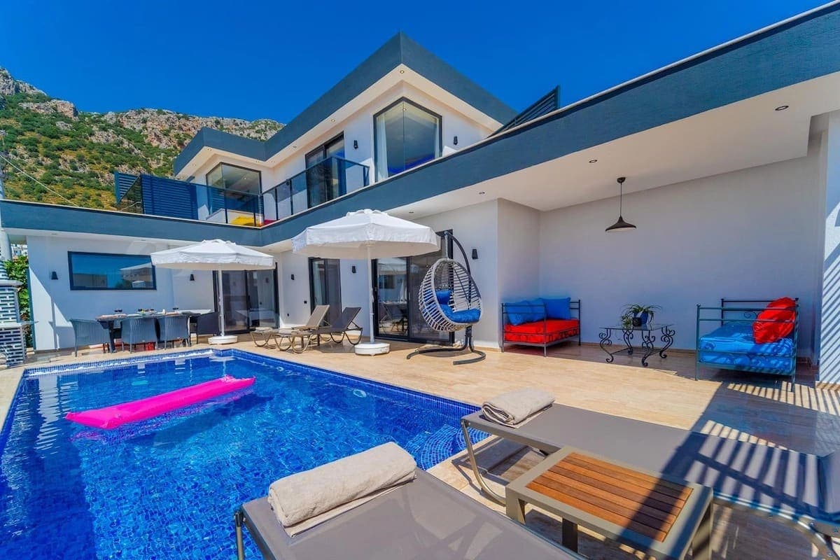 Havuz kenarında şezlonglar, salıncak, yemek masası ve oturma grubu bulunan modern bir villa.