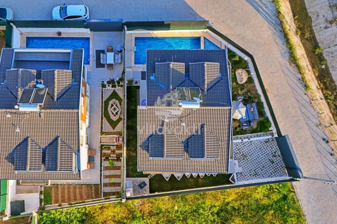 Havuzlu ve güneş panelli iki villanın kuş bakışı görünümü, bahçe düzenlemesi ve otopark alanı.