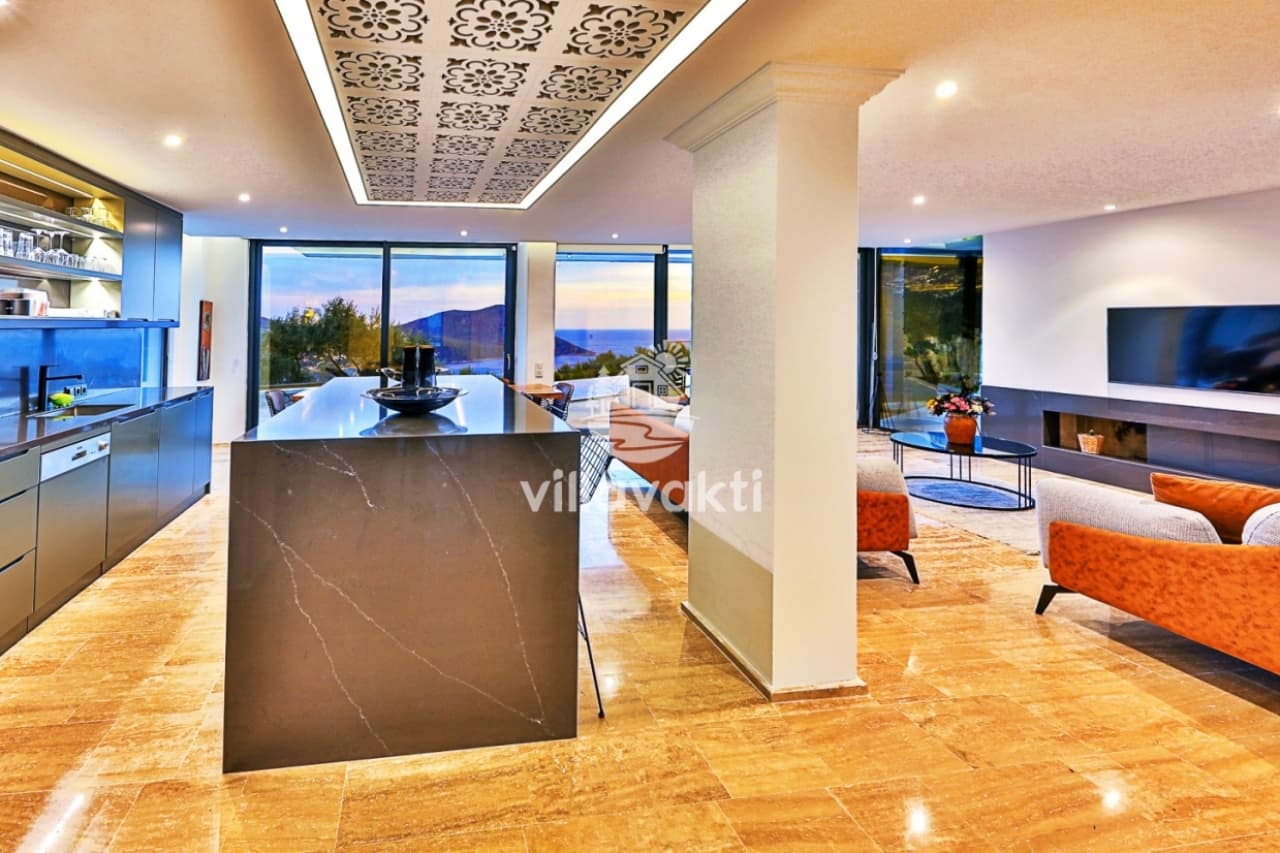 Modern mutfak adası, oturma grubu ve deniz manzaralı geniş cam pencereleri olan açık plan salon.