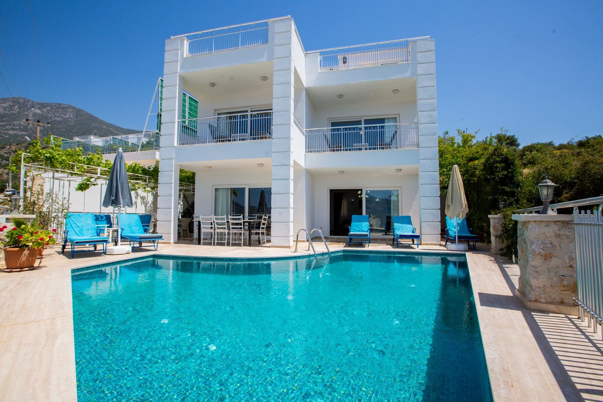 Önünde özel havuzu, güneş şezlongları ve yemek masası bulunan iki katlı beyaz modern villa.