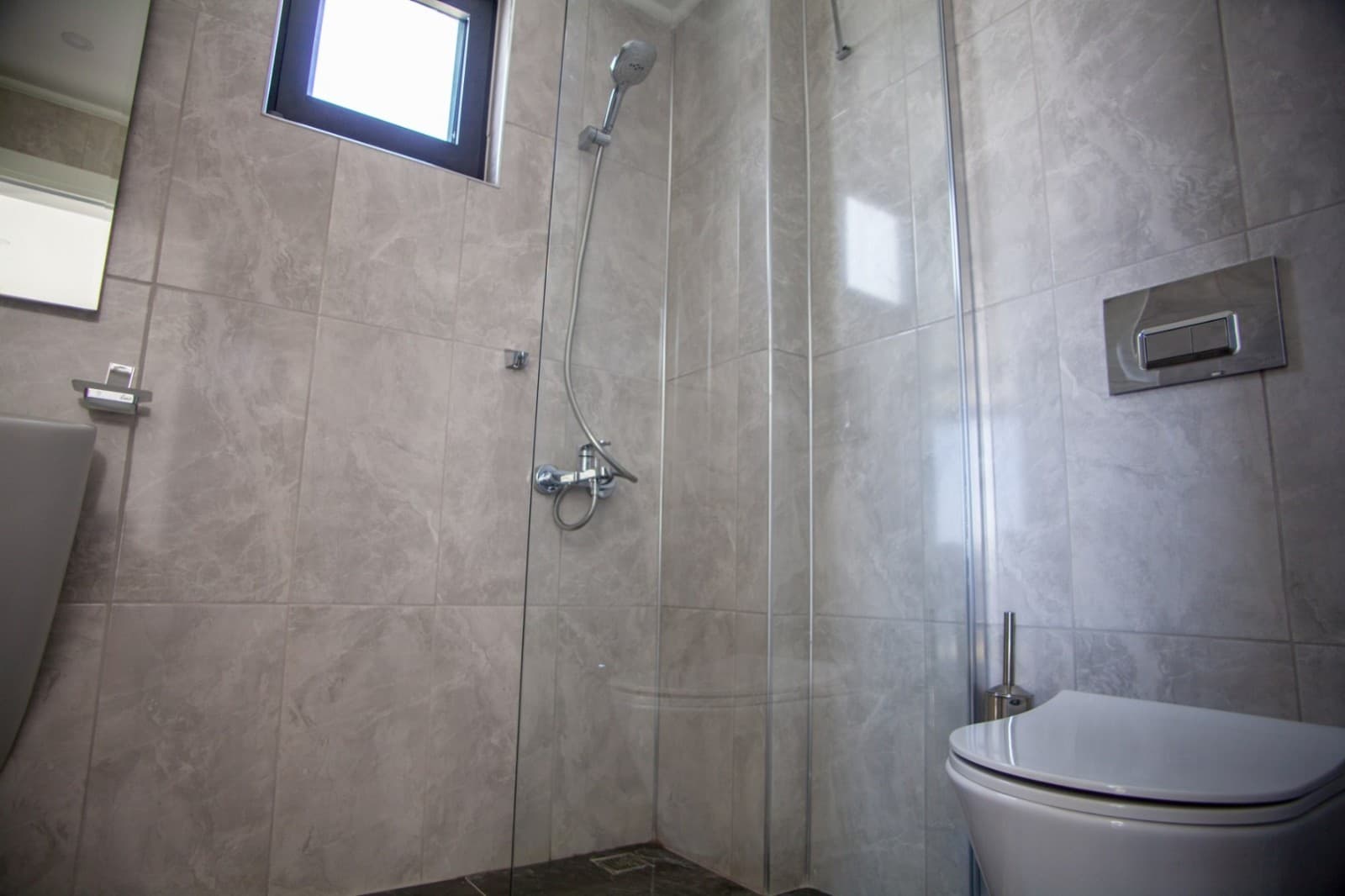 Gri mermer duvarlı duşakabin ve asma klozet bulunan banyo.