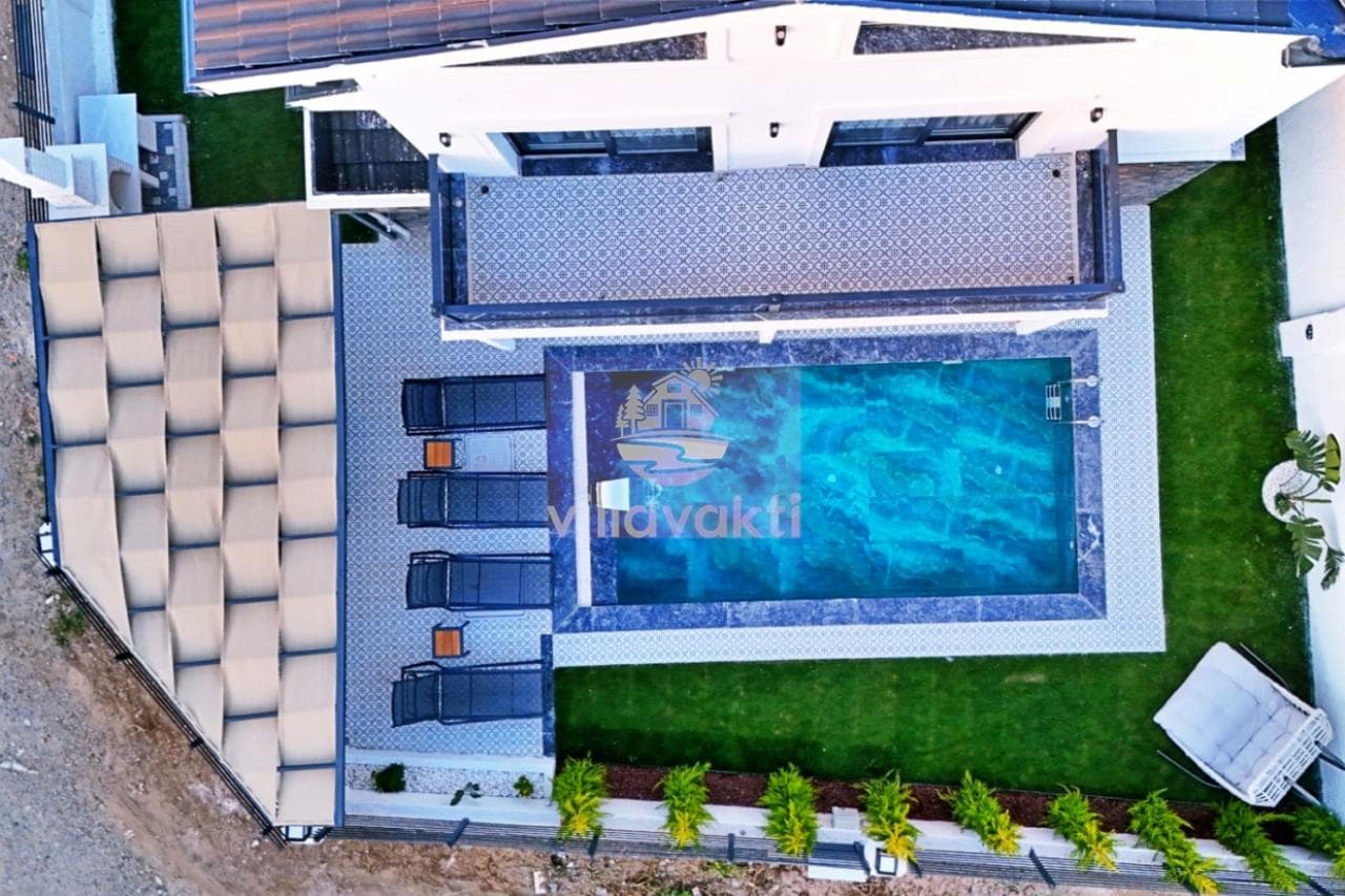 Üstten görünümle havuzlu villa bahçesi, şezlonglar, gölgelikli oturma alanı ve yeşil çimler.