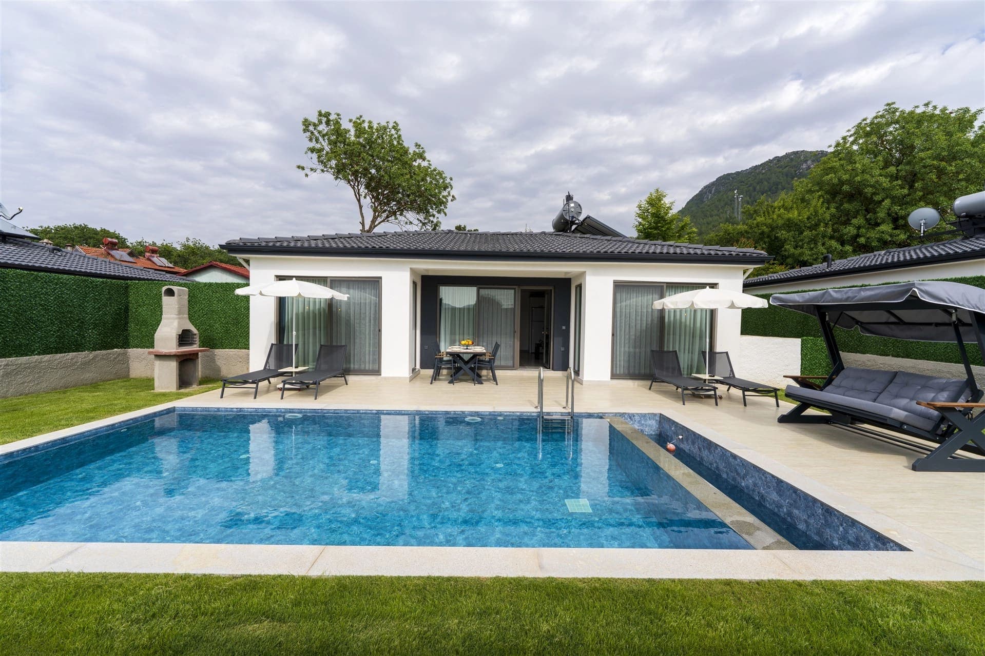 Bahçesinde havuz, şezlonglar, salıncak ve barbekü bulunan tek katlı beyaz villa.