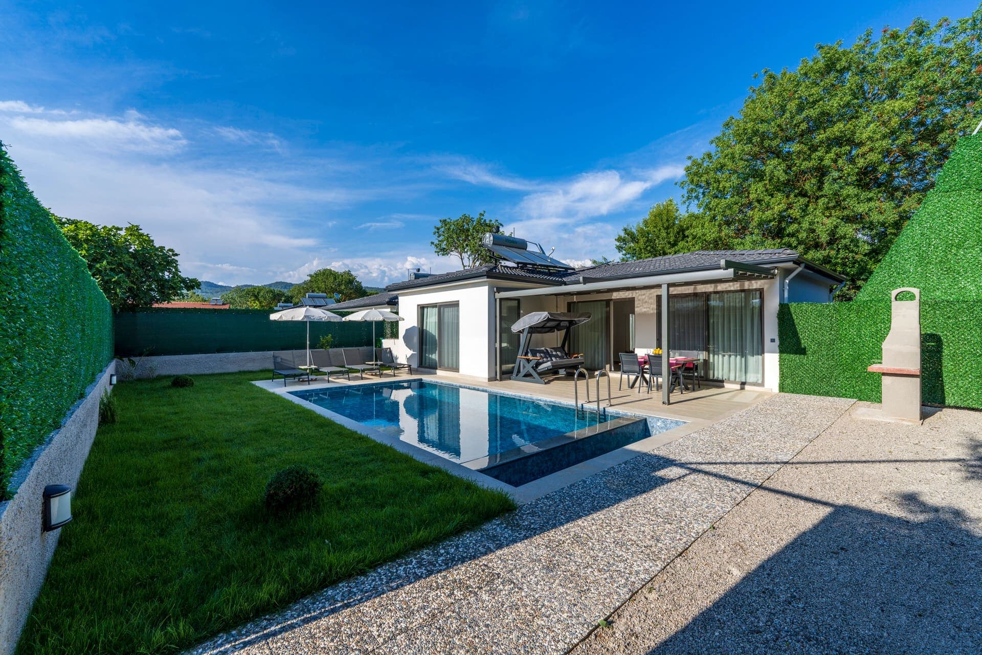 Yeşil çim bahçesi, havuzu ve barbeküsü olan tek katlı modern villa.
