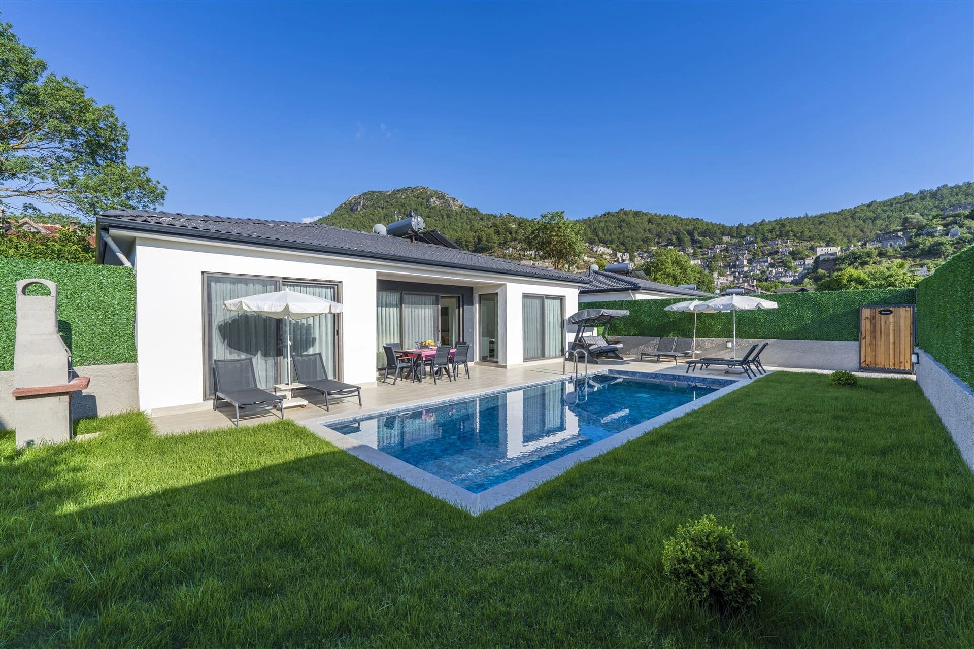 Dağ manzaralı bahçesinde havuz, şezlonglar ve barbekü bulunan tek katlı villa.