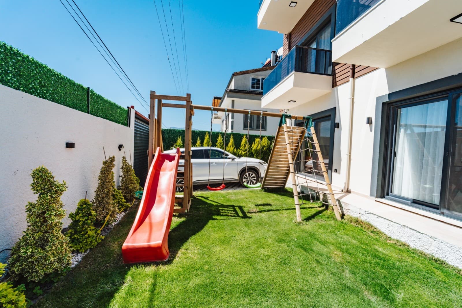 Bahçede kırmızı kaydırak ve salıncak bulunan çocuk oyun alanı.